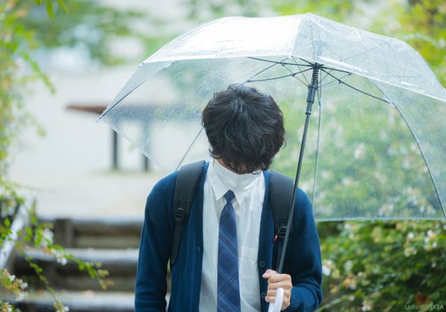 雨の中傘をさす高校生